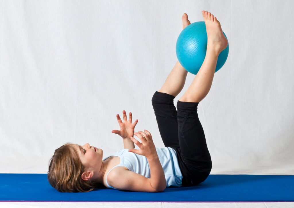 girl in white shirt and black pants lying on blue exercise ball