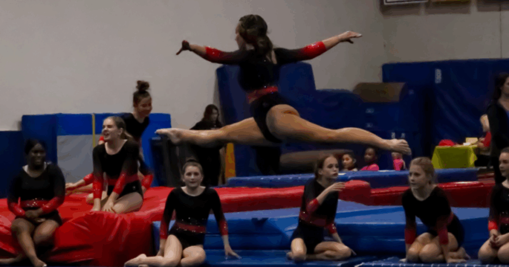 FlipZone gymnasts perform a split leap during a team practice experience while teammates watch and prepare for their turns during training.