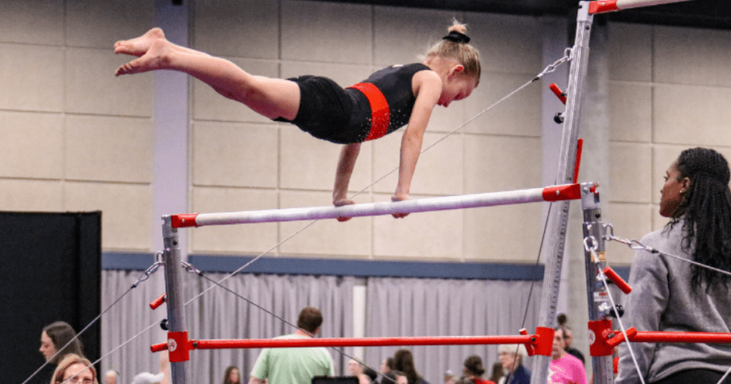 Young gymnast performs a straight-body hold on uneven bars during gymnastics team training, showing skills used in competitive gymnastics programs.