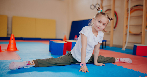 Young child practicing a gymnastics which is benefits for kids and great child development stretch on a padded mat in a kids gymnastics facility
