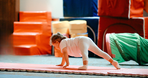 Young child practicing a beginner preschool gymnastics movement on a padded mat during a preschool gymnastics class